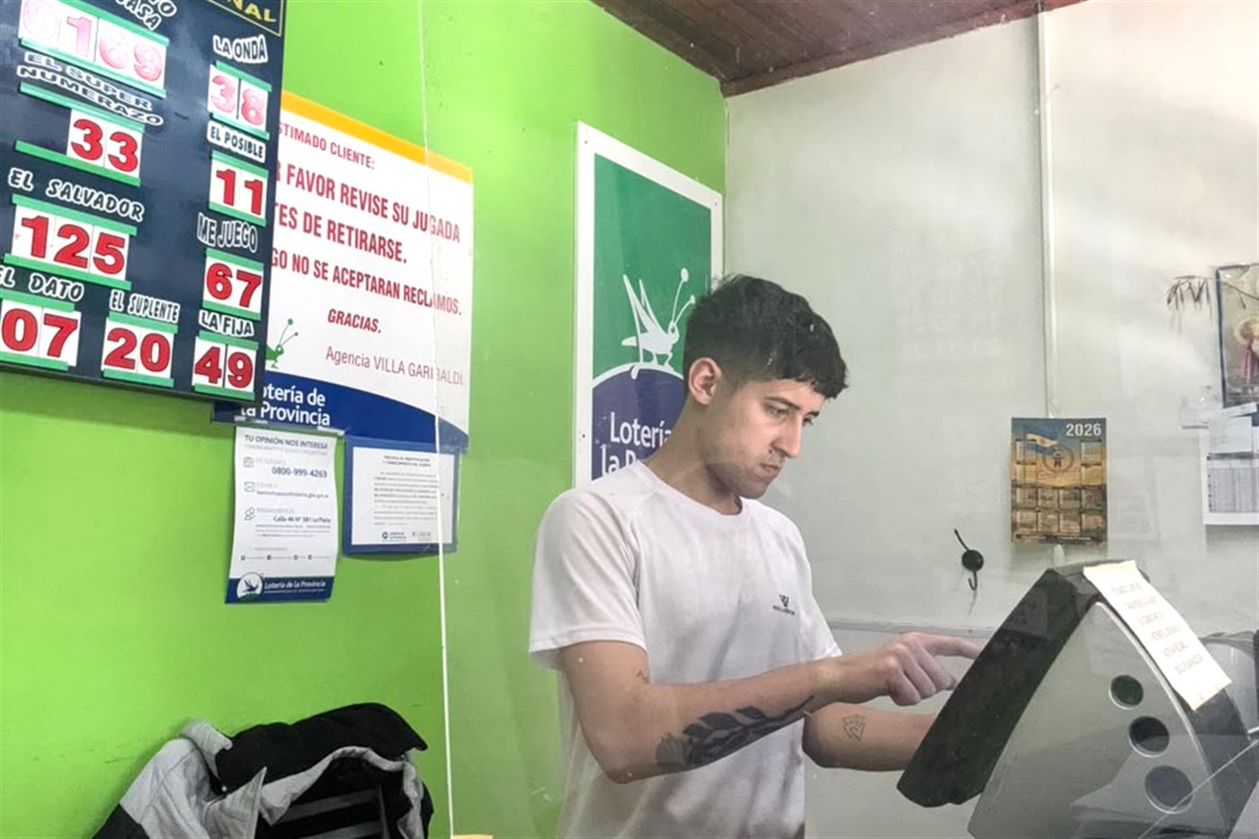 Kevin de pie cargando una jugada en la terminal, con el pizarrón de números detrás.
