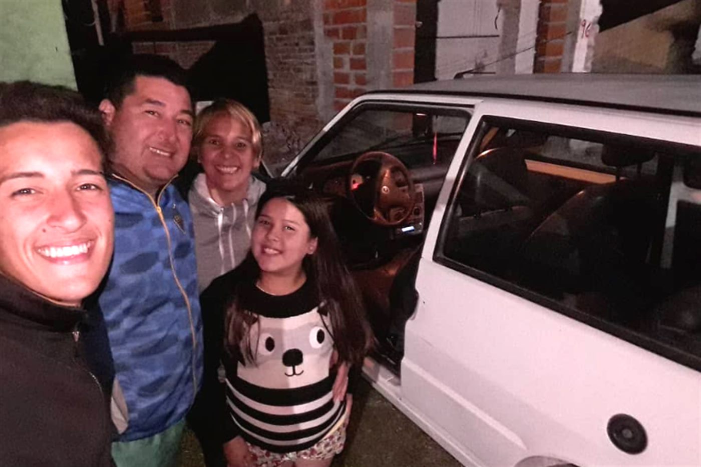 Kevin con su papá, su mamá y su hermana, parados al lado del Fiat Uno blanco.