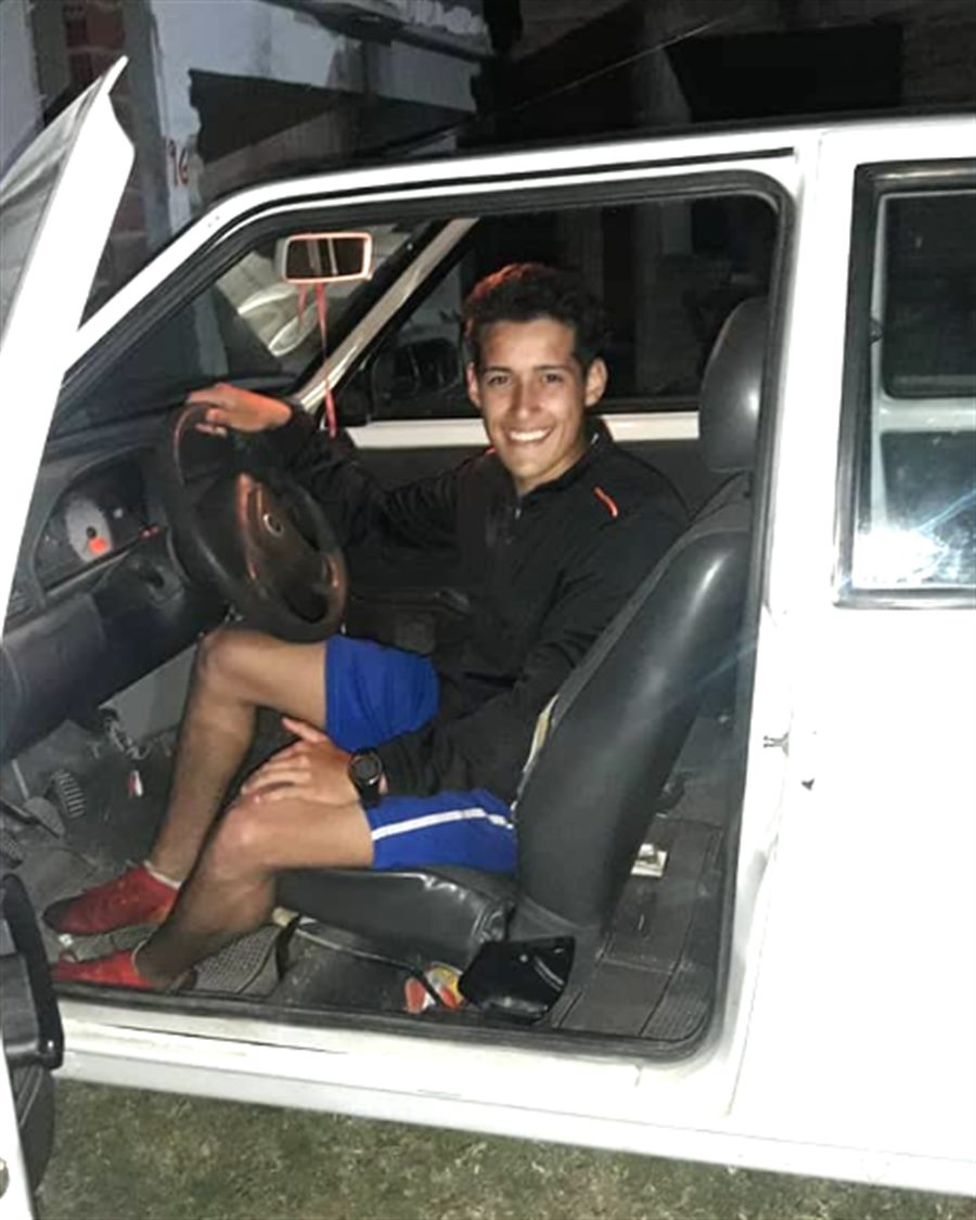 Kevin sentado al volante del Fiat Uno blanco, con la puerta abierta, de noche.