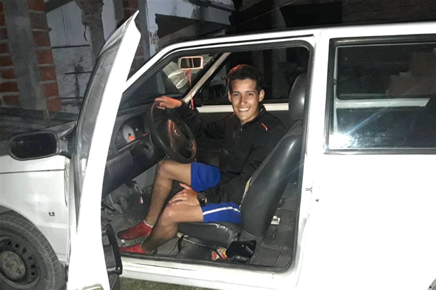 Kevin al volante del Fiat Uno blanco, con la puerta abierta, de noche.