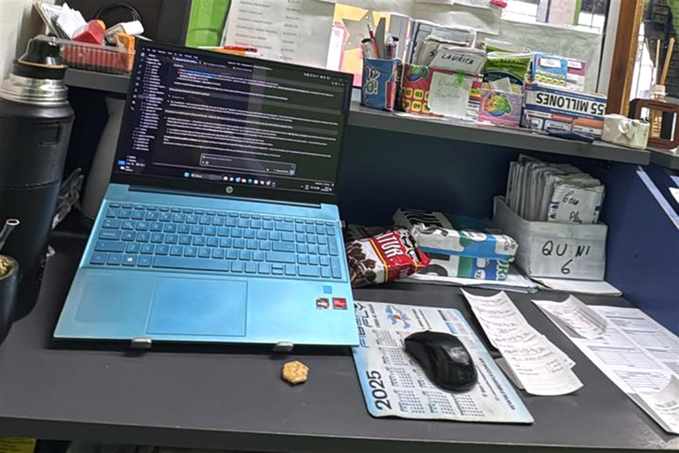 Una laptop con código abierto sobre el mostrador de la agencia, entre boletas de quiniela.