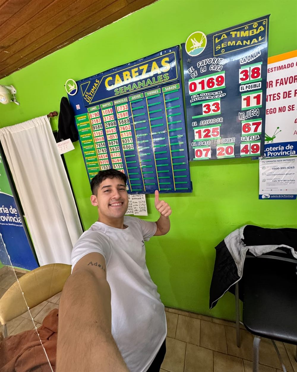 Kevin señalando el pizarrón de cabezas semanales de la agencia, con los números ganadores de cada sorteo.